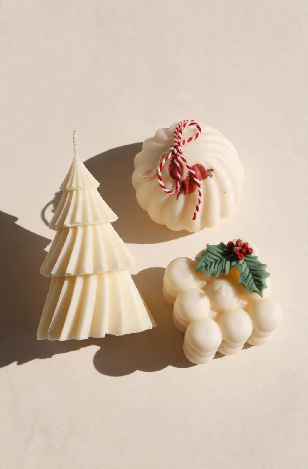 Tres velas navideñas claras: árbol geométrico y dos diseños redondeados con detalles festivos